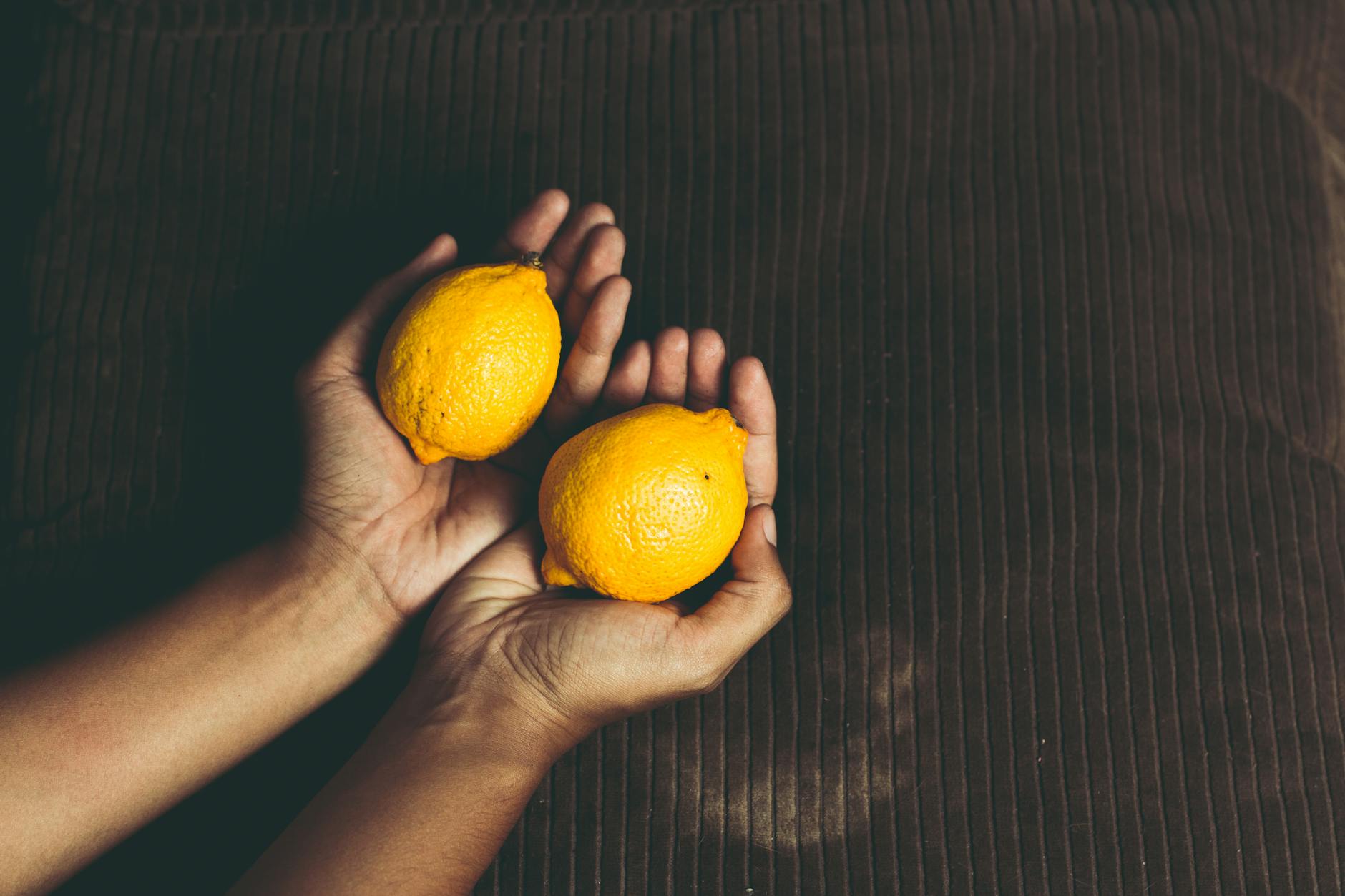 Close-up of two fresh lemons held in cupped hands, symbolizing renewal and freshness.