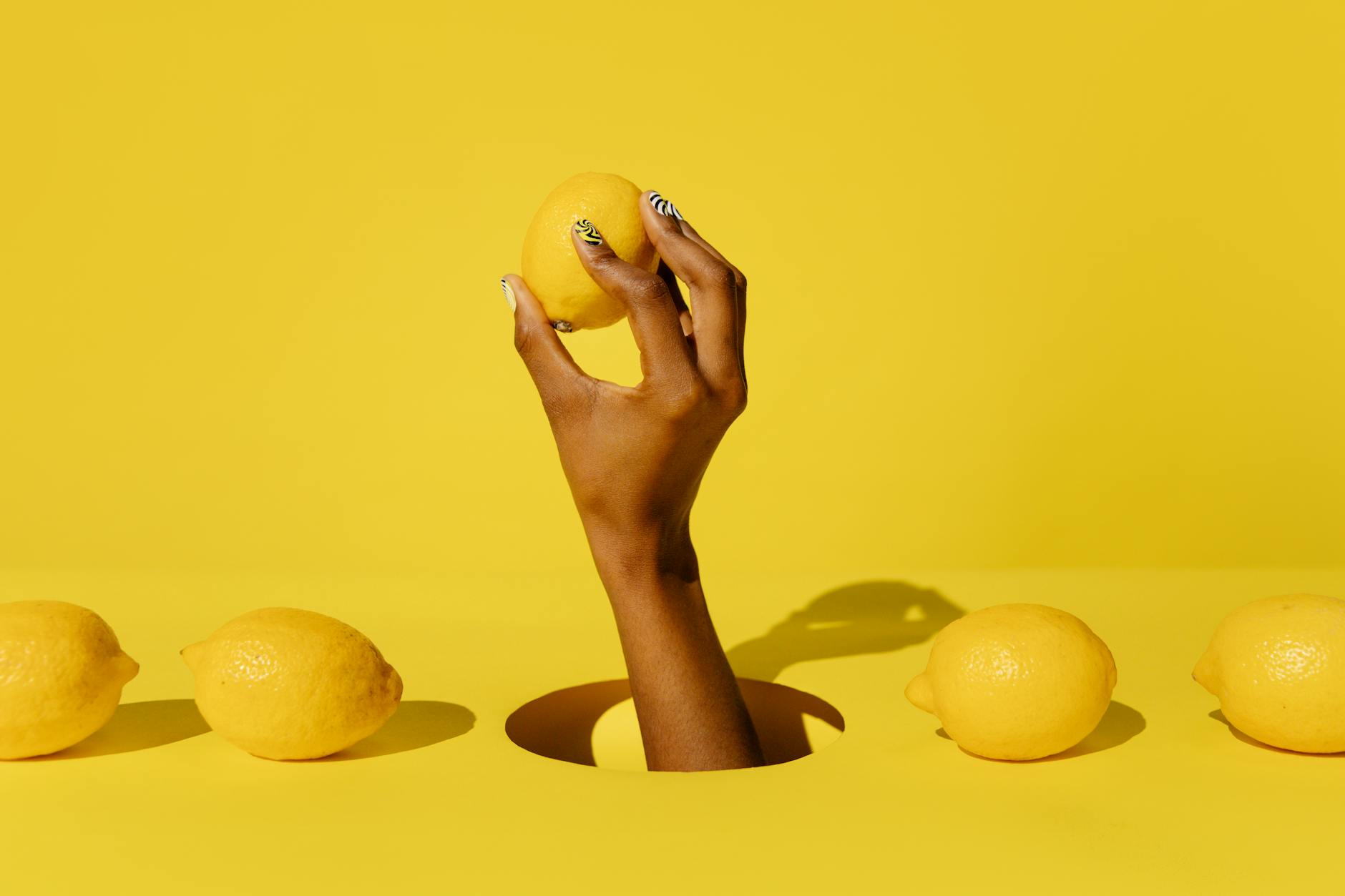 A hand holding a fresh lemon against a bright yellow background, symbolizing the gentle, focused approach to pleasure with clitoral vibrators