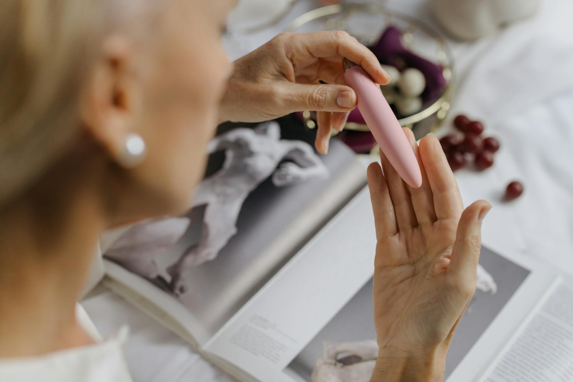 Close-up of a woman holding a pink vibrator, with art books in the background, emphasizing intimate pleasure