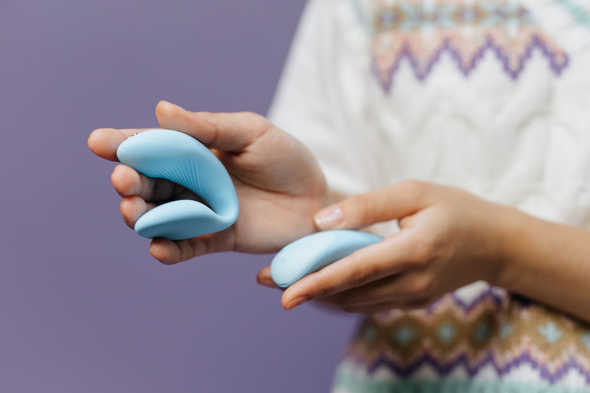 Hands holding a sleek blue vibrator against a purple background, symbolizing intimate exploration.