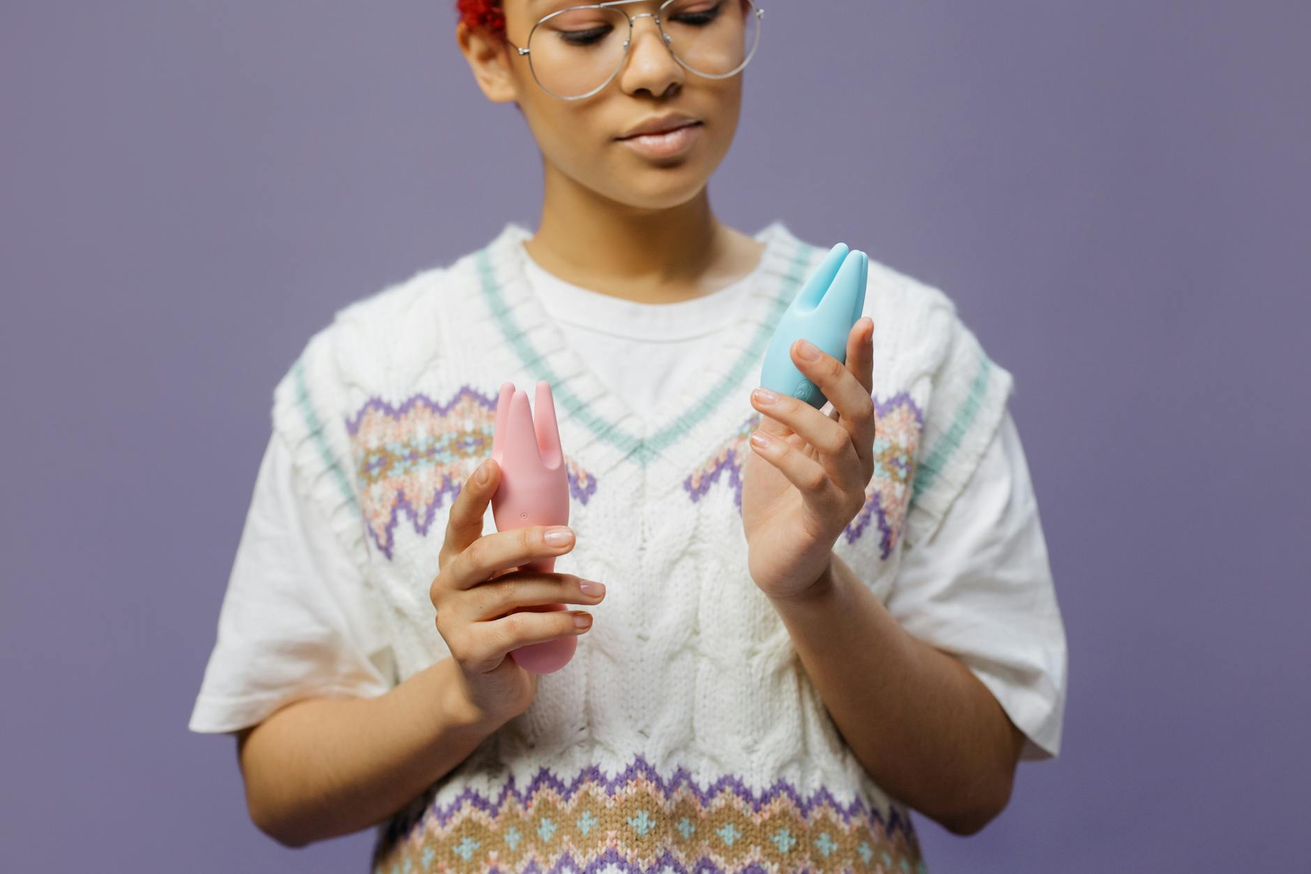 Woman holding blue and pink vibrators in contemplative moment