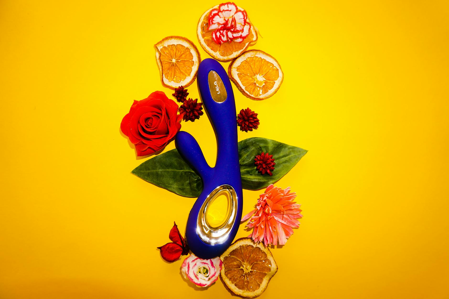 Lemon clitoral vibrator surrounded by flowers and citrus on yellow background